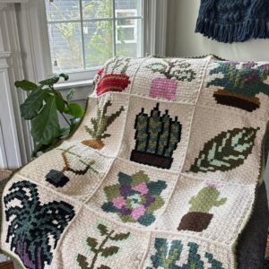 Plant-themed C2C (corner to corner) crochet blanket displayed on a recliner chair near a window.