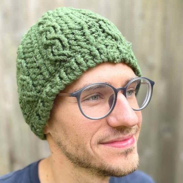 Green crochet beanie hat with cables modeled by a man with glasses