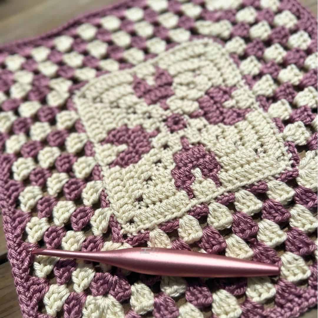 Crochet heart granny square with purple and cream yarn, perfect for cozy projects.
