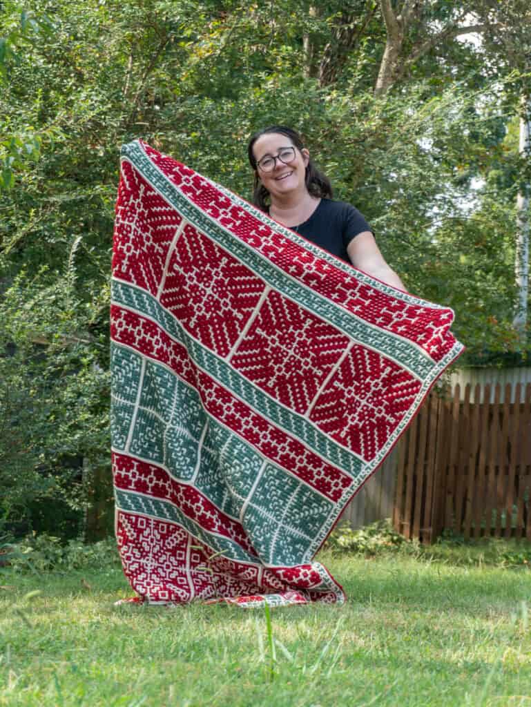 Woman holding a colorful patterned rug outdoors in a garden setting.